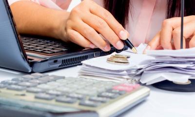 Accountant holding a pen calculating finances next to a laptop and calculator