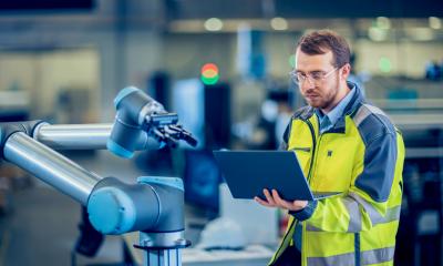 Automation engineer uses laptop for programming robotic arm