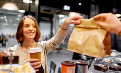A happy female customer with coffee cup taking paper bag from man in a vegan cafe
