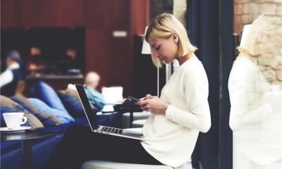 A modern business woman working on smart phone and laptop computer in a coffee shop