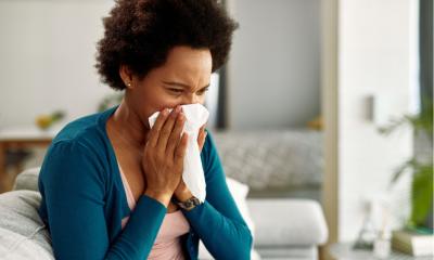 African American woman with flu virus blowing her nose at home