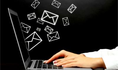 Hands type on a laptop while message icons fly from the screen - email concept.