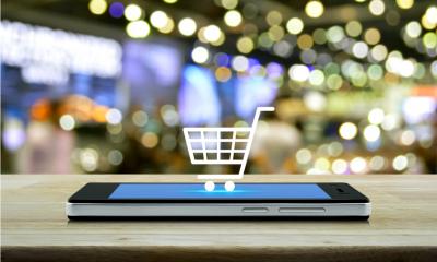 A mobile phone lying face up on a table with a website showing a shopping trolley on the screen
