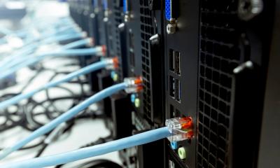 Rows of computers with blue cables going into them with other IT equipment in the background