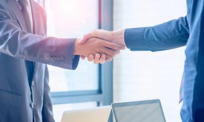 Two men in suits shaking hands over a desk