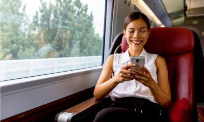 Woman sitting down on a train smiling while working using her mobile phone