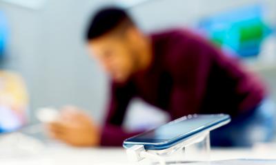 Man using a mobile device in a phone shop with another device in the foreground