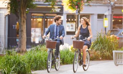 Businesswoman And Businessman Riding Bike Through City Park