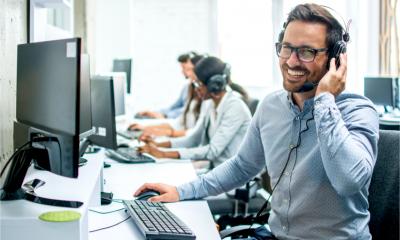 A smiling male tech support operator takes a call from a customer.