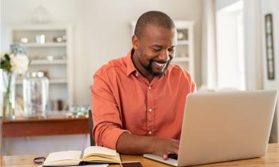 Man in an orange shirt sat at home using his laptop to do freelance work