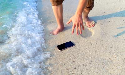 A man has dropped his phone on the beach and the waves are about to make it wet