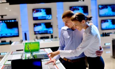 A young couple in an electronics store look at a new laptop on display