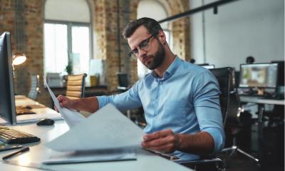 bearded engineer in eyeglasses and formal wear looking at blueprint while working in the office